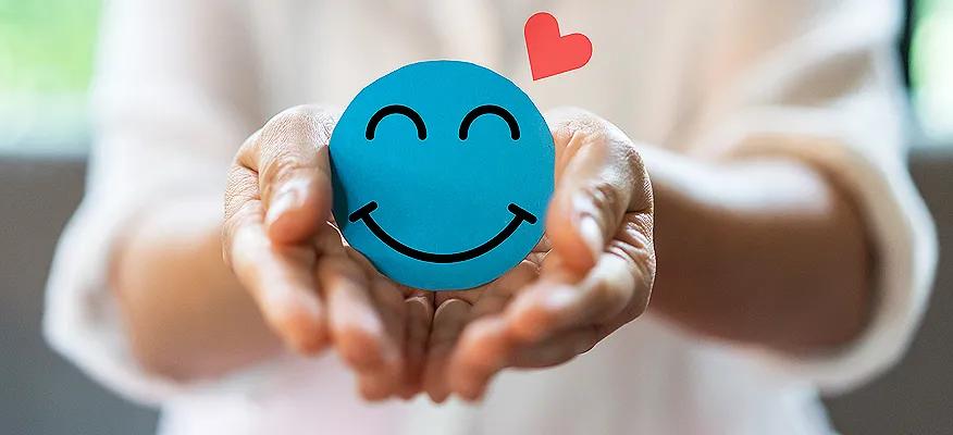Smiling blue stress ball with heart in hands, a concept image for what is emotional health.