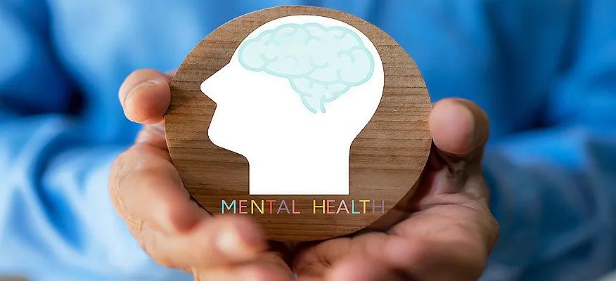 A person holding a wooden circle with a brain icon, symbolizing awareness of what is mental health.