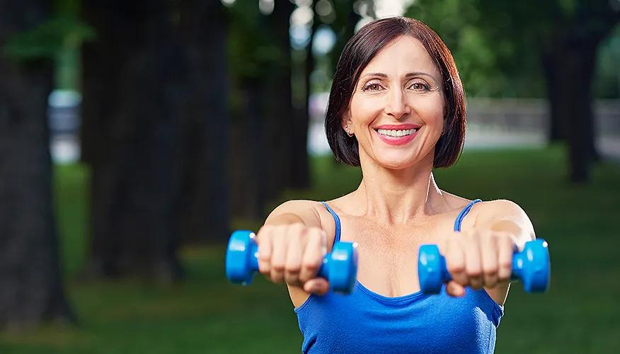 Woman exercising outdoors with blue dumbbells, fitness and healthy lifestyle.