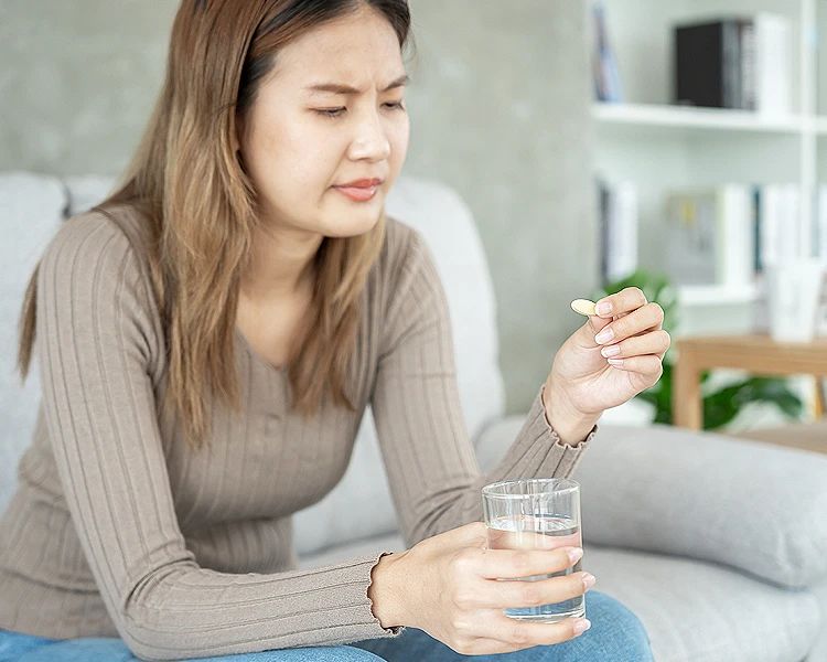 Woman taking vitamin supplement for stress and anxiety with glass of water at home